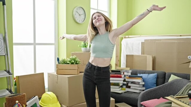 Young blonde woman smiling confident standing with arms open at new home