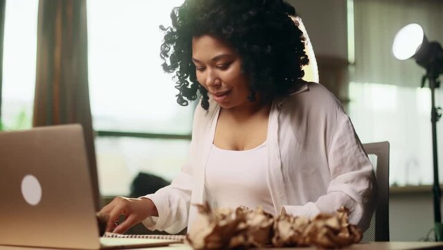 Portrait of positive young woman juggles crumpled papers with failed ideas while finding solution and writing in notebook with happy inspired face at home Idea pointing forward index finger concept