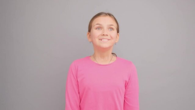 A girl in a pink sweater on a gray background thinks and looks up and to the side.