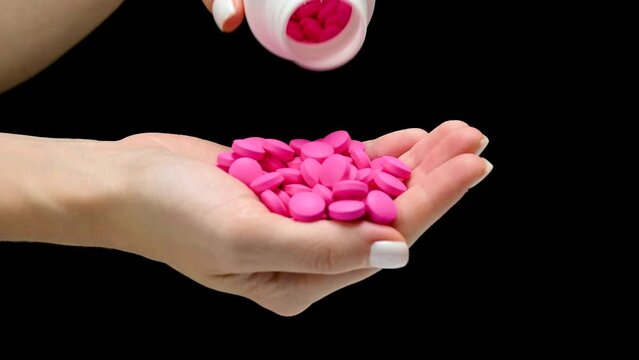 White jar of pills pours pink pills in hand on blck background isolation