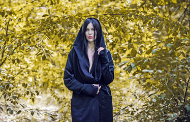 Woman with dark long hair in black, gothic style, black robe. Mysterious portrait in forest