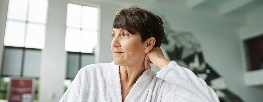 relaxed pose, joyful mature woman in white robe looking away, indoor spa center, tranquil, banner