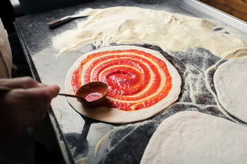 A man spreads Italian tomato paste over the dough, part of the pizza preparation process at the family café