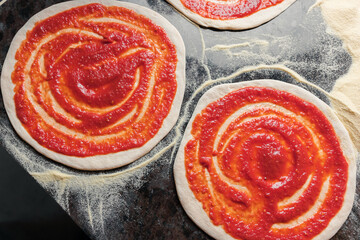 A woman adds tomato paste to the dough, preparing pizza for baking in a restaurant