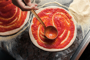 A woman adds tomato paste to the dough, preparing pizza for baking in a restaurant