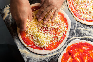 An Italian chef adds and spreads cheese over dough with tomato paste