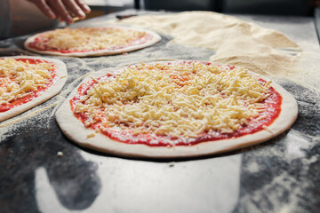 An Italian chef adds and spreads cheese over dough with tomato paste