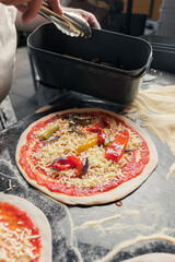 An experienced chef adds vegetables to the pizza after adding tomato paste and cheese to the dough