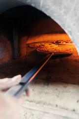 A talented French chef places a cheese and sausage pizza into the hot oven for 5 minutes