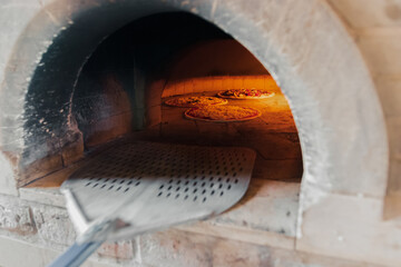 A talented French chef places a cheese and sausage pizza into the hot oven for 5 minutes