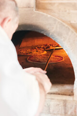 A talented French chef places a cheese and sausage pizza into the hot oven for 5 minutes