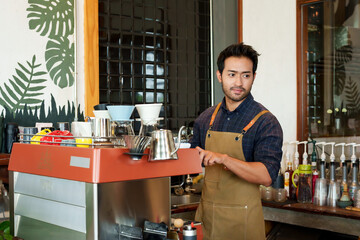 Fototapeta premium Portrait Nice-looking Asian man wh owns shop wearing apron, man standing making coffee according order that customer ordered standing in front coffee machine that can do all coffee menu...