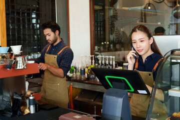 Beautiful Asian coffee shop owner is taking orders from Roo on the phone. and tell her husband to make a cappuccino to prepare to send to customers. Indian women and men Worked in a small coffee shop.