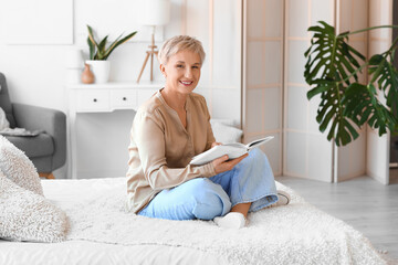 Mature woman reading book in bedroom