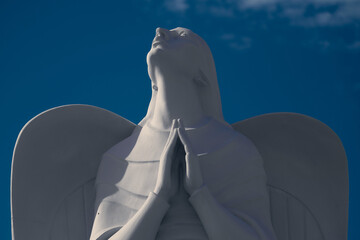 Angelic Statue in Prayer: Graceful Sculpture amidst Ethereal Clouds