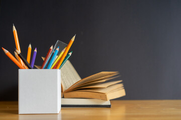 close up on pencil with school supplied and opened book on black chalkboard background for back to school concept