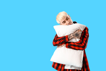 Young tattooed man with soft pillow on blue background