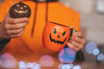 Portrait of candid authentic zoomer boy posing with jack lantern mug and sweets at halloween party