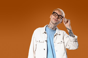 Young tattooed man in stylish eyeglasses on color background