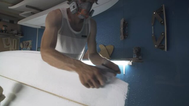 Male surfboard shaper making surfboard in his workshop. Hand shaping from blank.