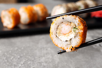 Chopsticks with tasty sushi roll, closeup view