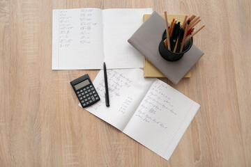 Open copybook with math formulas and calculator on wooden table