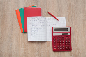 Open copybook with math formulas and calculator on wooden table