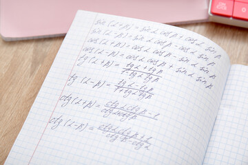 Open copybook with math formulas on wooden table, closeup