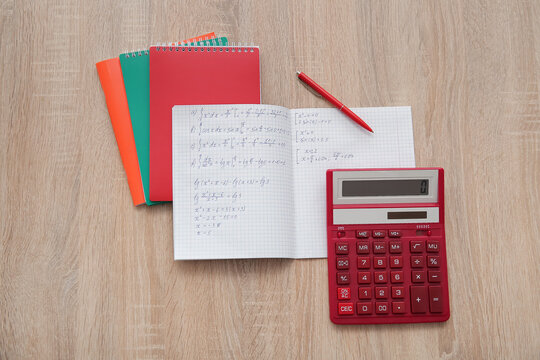 Open copybook with math formulas and calculator on wooden table