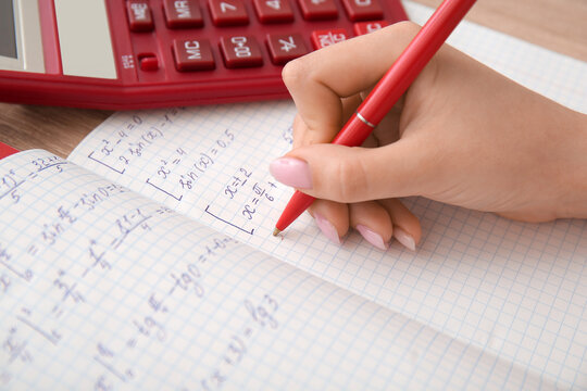 Woman writing math formulas in copybook on wooden table, closeup