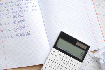 Calculator and copybook with math formulas on wooden table