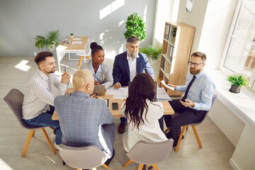 Multiracial coworkers have working together at office meeting. View from above of diverse business people in formal wear sitting at desk working on project, discussing financial documents