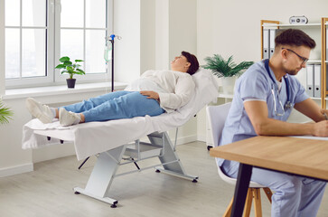 Fat young woman lying in doctor's office on the couch in clinic and receiving IV drip infusion or...