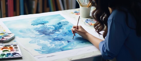 A girl at home creates artistic artwork using blue gouache on cardboard