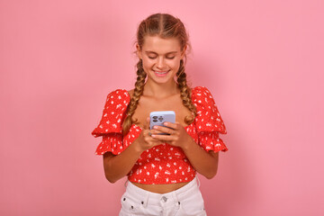 Young beautiful Caucasian woman teenager in glasses holds smartphone and smiles looking at camera inviting to chat in new application for internet communications stands on pink studio background.