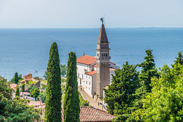 A view past trees towards the cathedral in the town of Piran, Slovenia in summertime © Nicola
