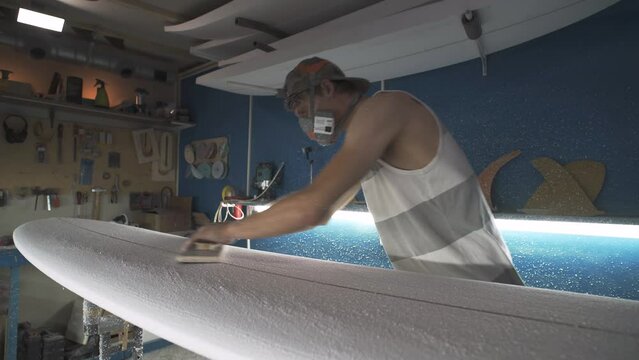 Male surfboard shaper making surfboard in his workshop. Hand shaping from blank.