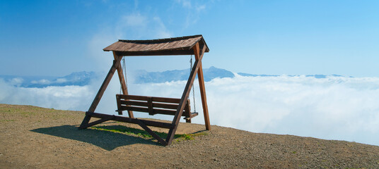 Swing without people over a precipice overlooking the clouds.