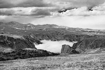 Panoramic alpine mountain view in classic black and white with fog settling in the valley below and storm clouds overhead in the Rocky Mountains of Wyoming.