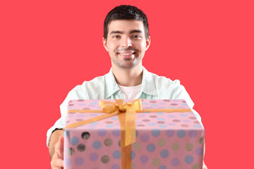Happy young man with birthday gift on red background