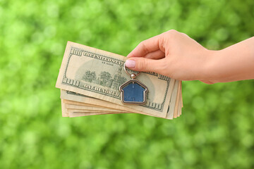Female hand holding trinket in house shape and money on decorative green grass background. Concept...