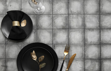 Elegant table setting with black plates, golden leaves and cutlery on grey tiled background