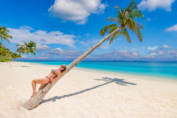Fototapeta na wymiar Happy young carefree traveler woman relaxing laying on coconut palm tree in bikini. Happy sunshine tropical sandy beach seascape, beautiful blue sky. Summer paradise vacation wallpaper. Wellbeing body