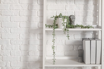 Shelf unit with plant and folders near white brick wall