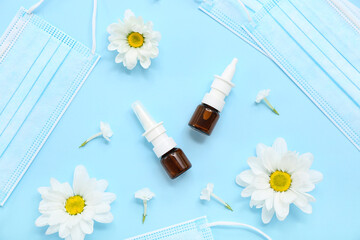 Bottles of nasal drops with daisy flowers and medical masks on blue background