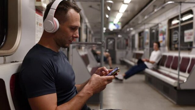 Young man using mobile phone while sitting on the subway train and listening to music