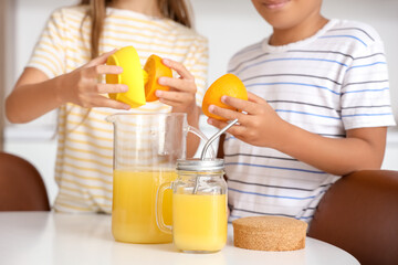 Little children making fresh orange juice at table in kitchen