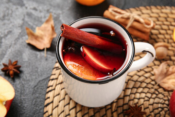 Cup of hot mulled wine with apple and orange on black background