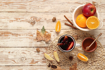 Cup of hot mulled wine with apple and orange on white wooden background
