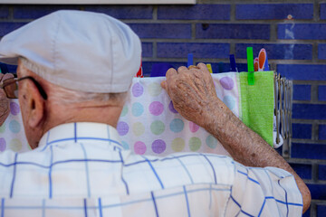 Active elderly doing housework. Unrecognizable retired man hanging up the laundry. Cooperation,...